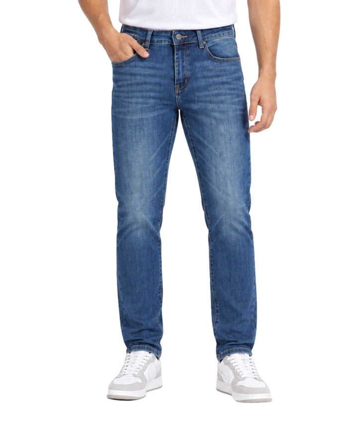 Hombre vistiendo jeans Jeanswest color azul medio stone con calzado blanco sobre fondo blanco.