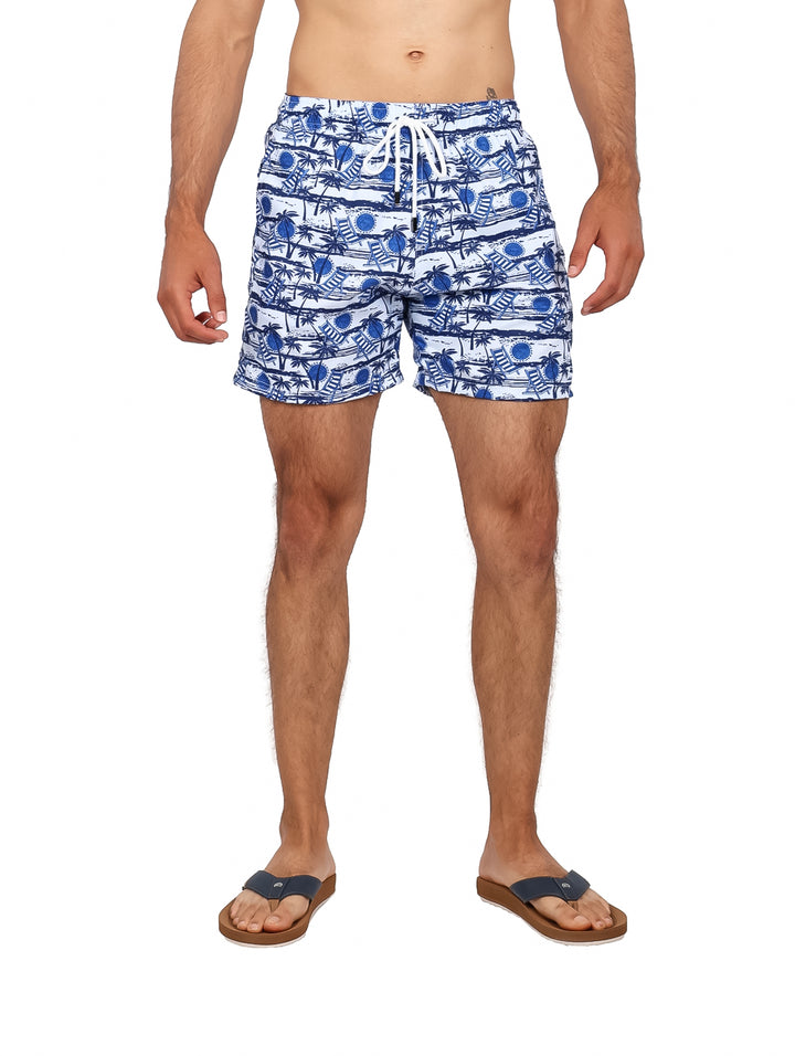 Hombre vistiendo traje de baño corto estampado en color azul marino y blanco con diseño de palmeras.
