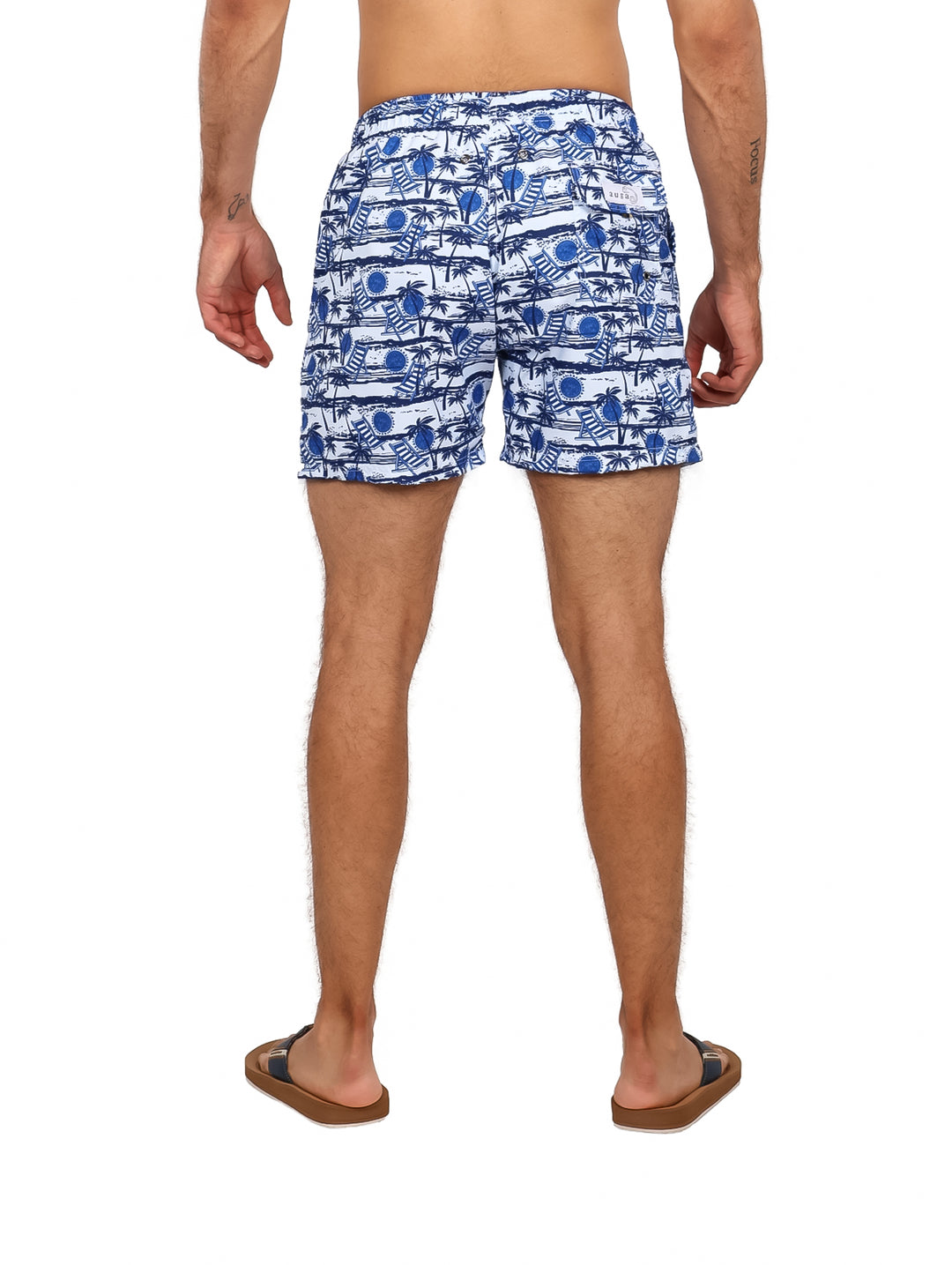 Hombre vistiendo traje de baño corto estampado en color azul marino y blanco con diseño de palmeras.