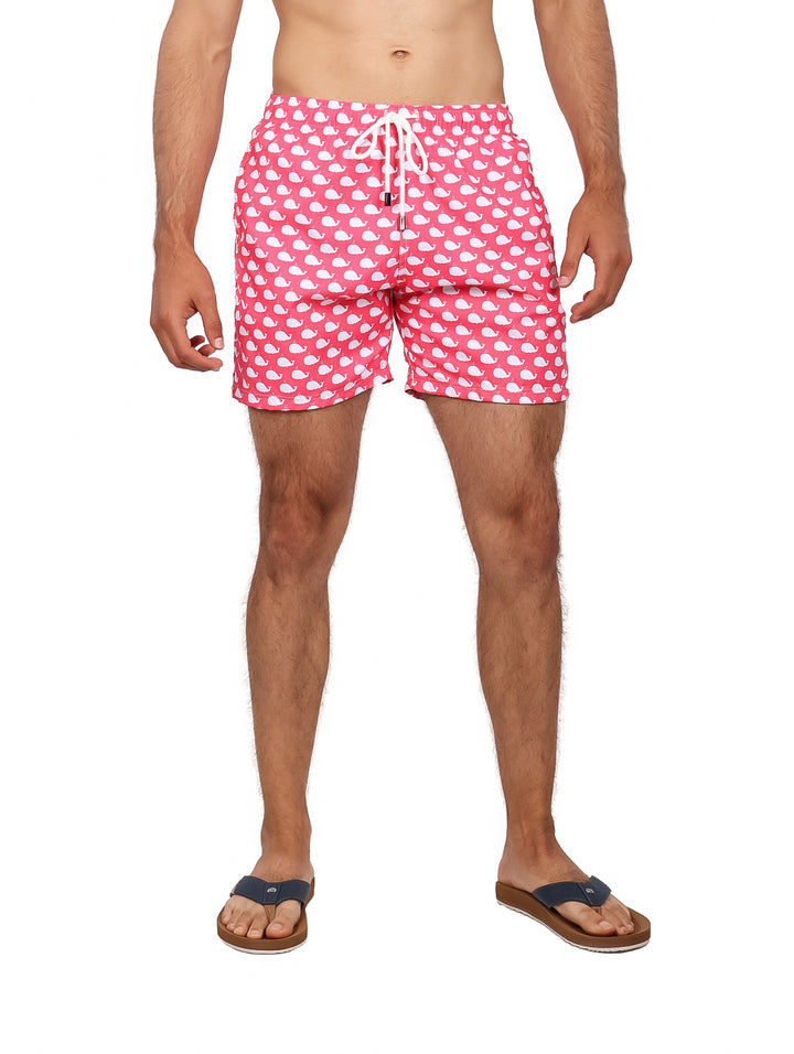 Hombre vistiendo un traje de baño corto color rosa con estampado de ballenas blancas.