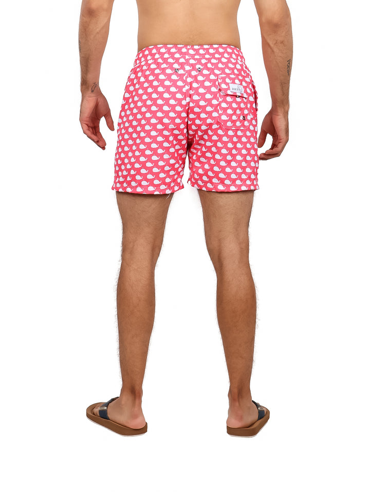 Hombre vistiendo un traje de baño corto color rosa con estampado de ballenas blancas.