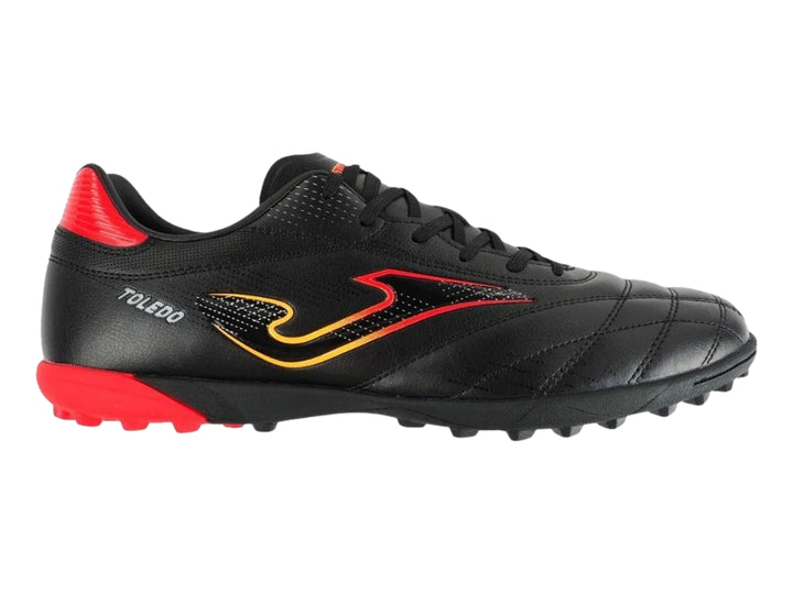 Zapato de fútbol Joma Toledo color negro con detalles en rojo y amarillo, diseño para superficie artificial.