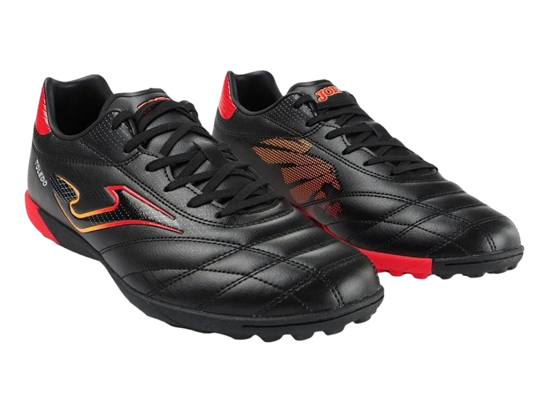 Zapato de fútbol Joma Toledo color negro con detalles en rojo y amarillo, diseño para superficie artificial.