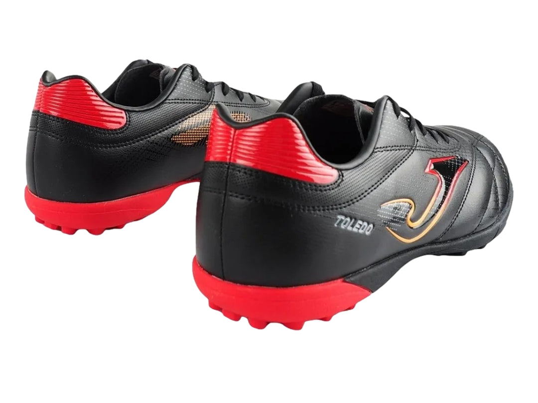 Zapato de fútbol Joma Toledo color negro con detalles en rojo y amarillo, diseño para superficie artificial.