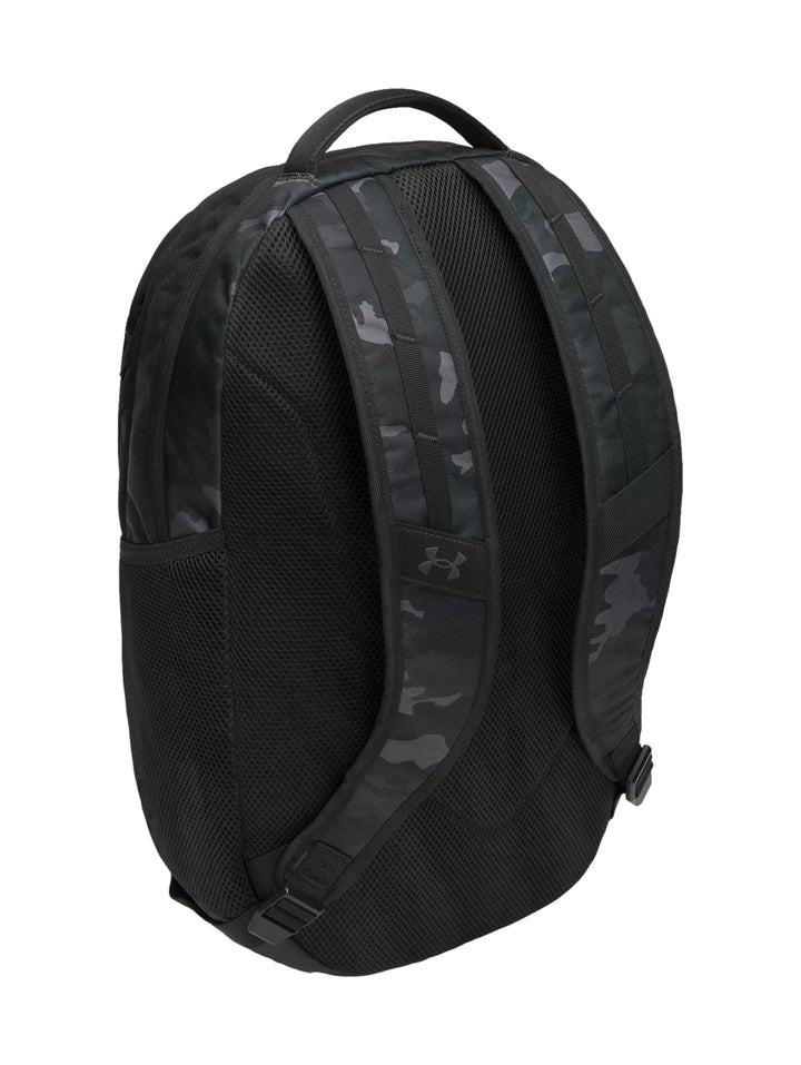 Mochila Under Armour negra con estampado de camuflaje y logotipo blanco frontal.