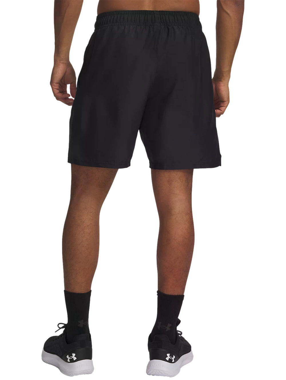 Hombre vistiendo shorts deportivos negros de Under Armour sobre mallas naranjas y tenis negros.