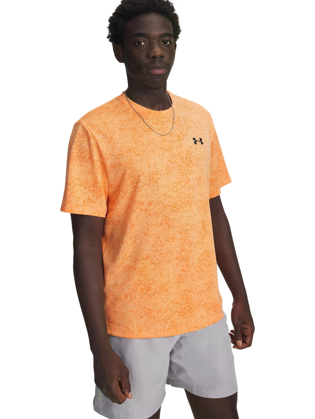 Hombre vistiendo playera deportiva Under Armour color naranja con patrón pixelado y shorts grises.
