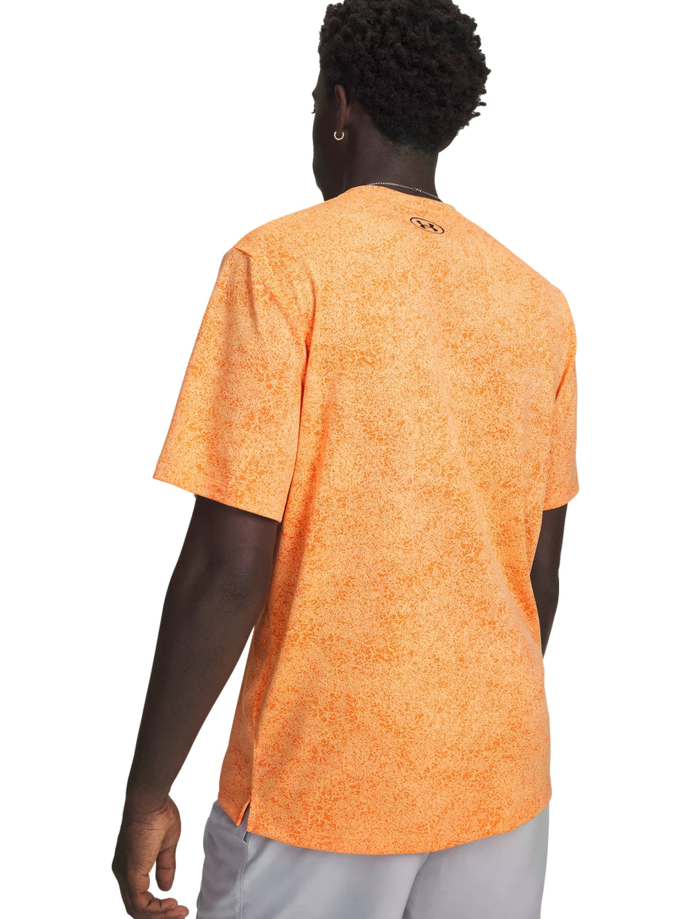 Hombre vistiendo playera deportiva Under Armour color naranja con patrón pixelado y shorts grises.