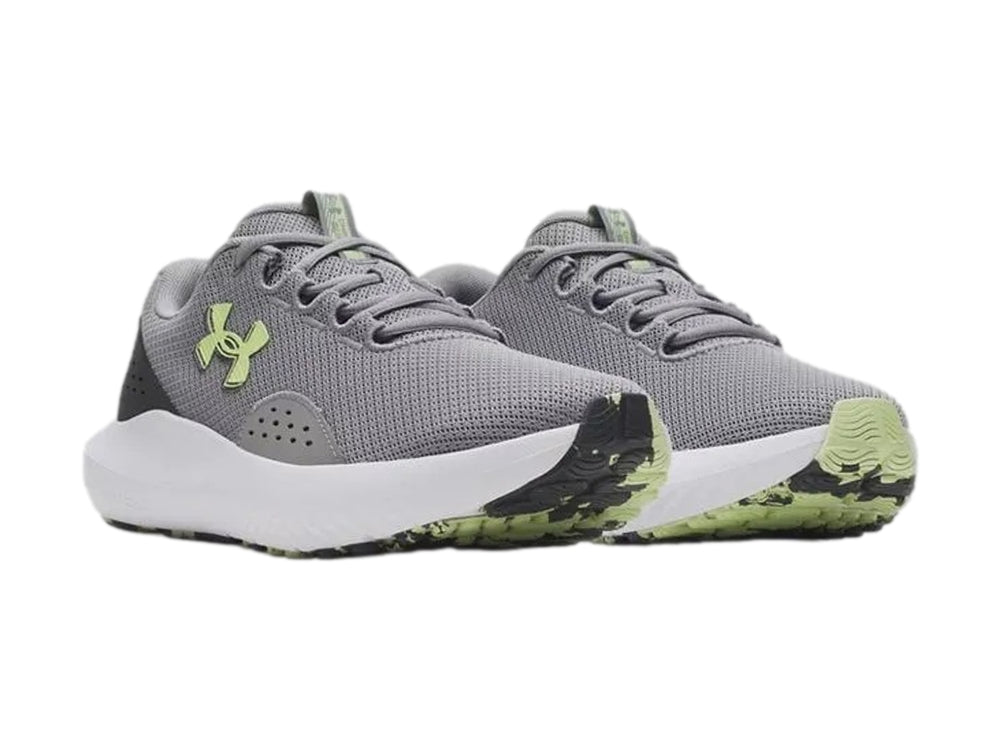 Tenis deportivos Under Armour Charged Surge 4 en color gris con suela blanca y logo en tono verde lima.