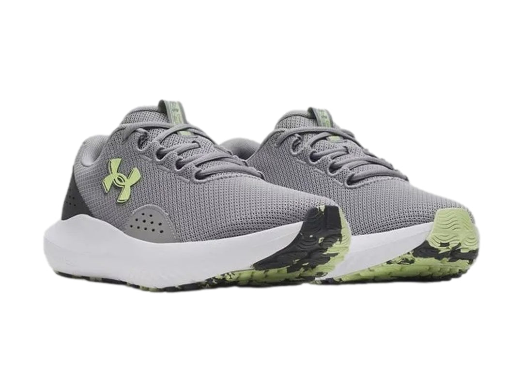 Tenis deportivos Under Armour Charged Surge 4 en color gris con suela blanca y logo en tono verde lima.