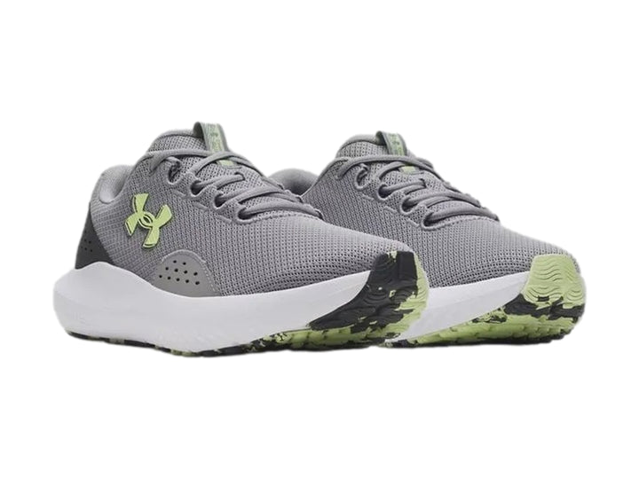 Tenis deportivos Under Armour Charged Surge 4 en color gris con suela blanca y logo en tono verde lima.
