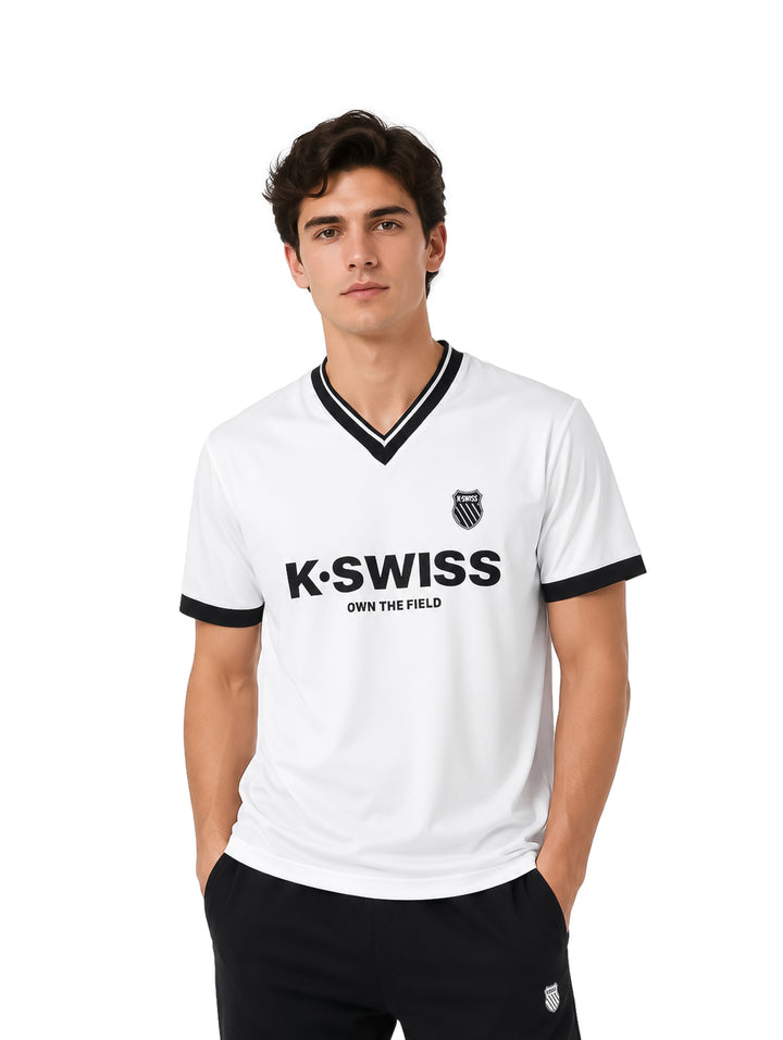 Hombre vistiendo playera blanca K-SWISS de manga corta con cuello en V y detalles en color negro.