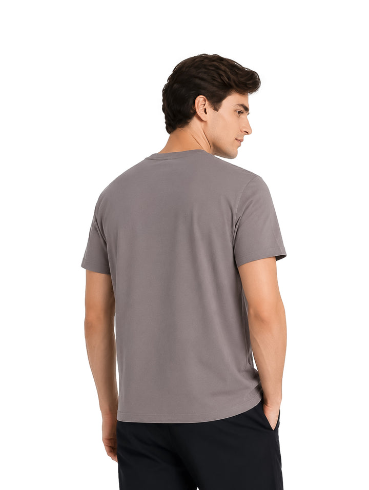 Hombre vistiendo playera K-Swiss color gris con detalle de texto negro en el pecho y pantalones negros.