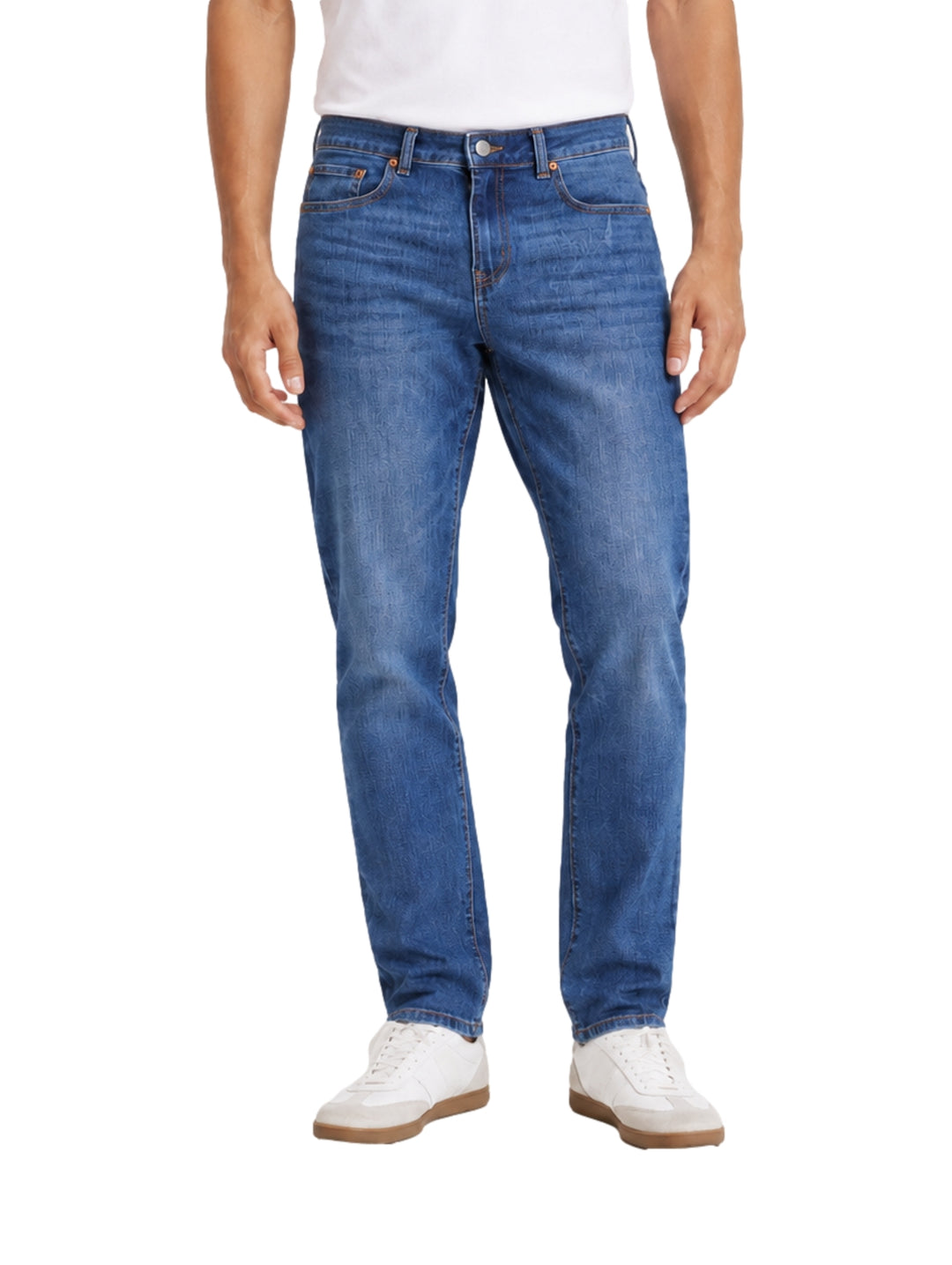 Hombre vistiendo jeans color azul oscuro con tenis blancos sobre fondo blanco.