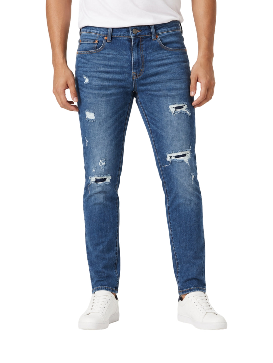 Hombre usando jeans de mezclilla azul medio con efecto roto y tenis blancos.