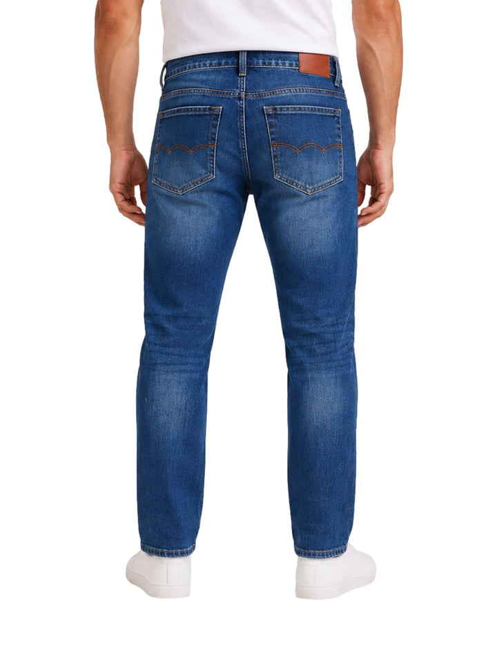 Hombre usando jeans de mezclilla azul medio con efecto roto y tenis blancos.