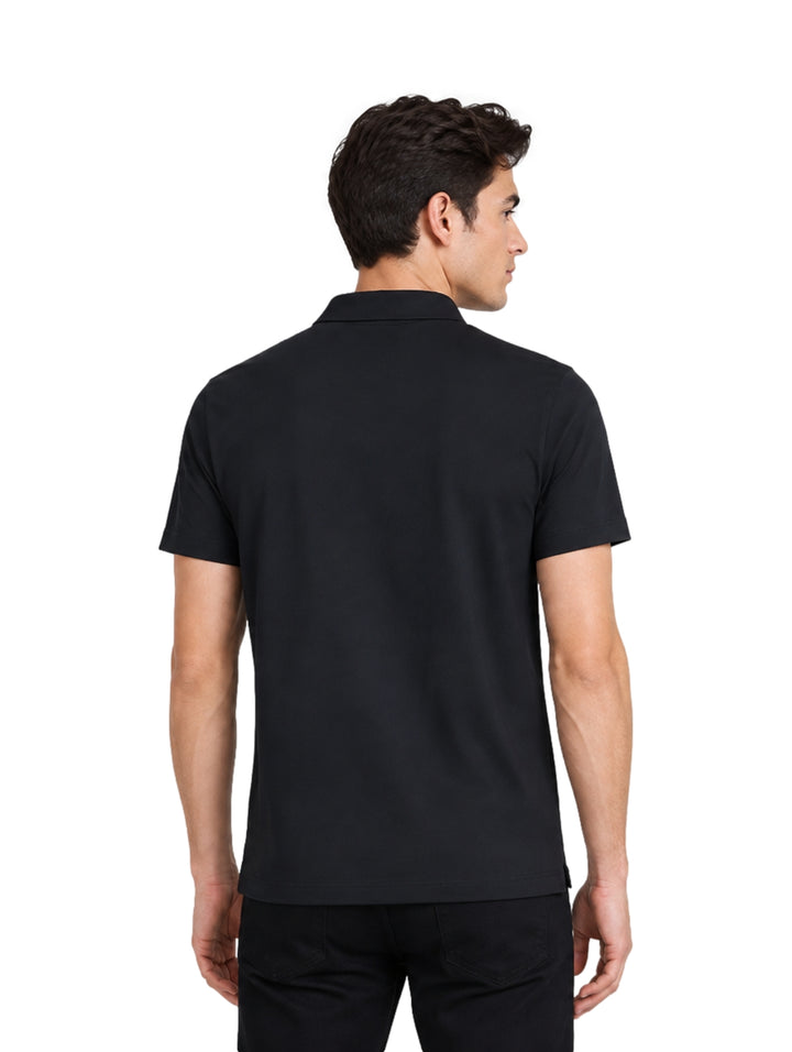 Hombre vistiendo una playera polo de color negro de manga corta y pantalones negros sobre fondo blanco.