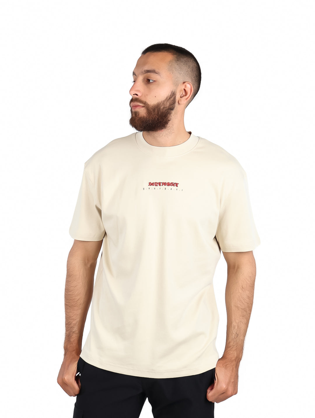 Hombre vistiendo una playera de color beige de manga corta con un pequeño logo rojo en el pecho.