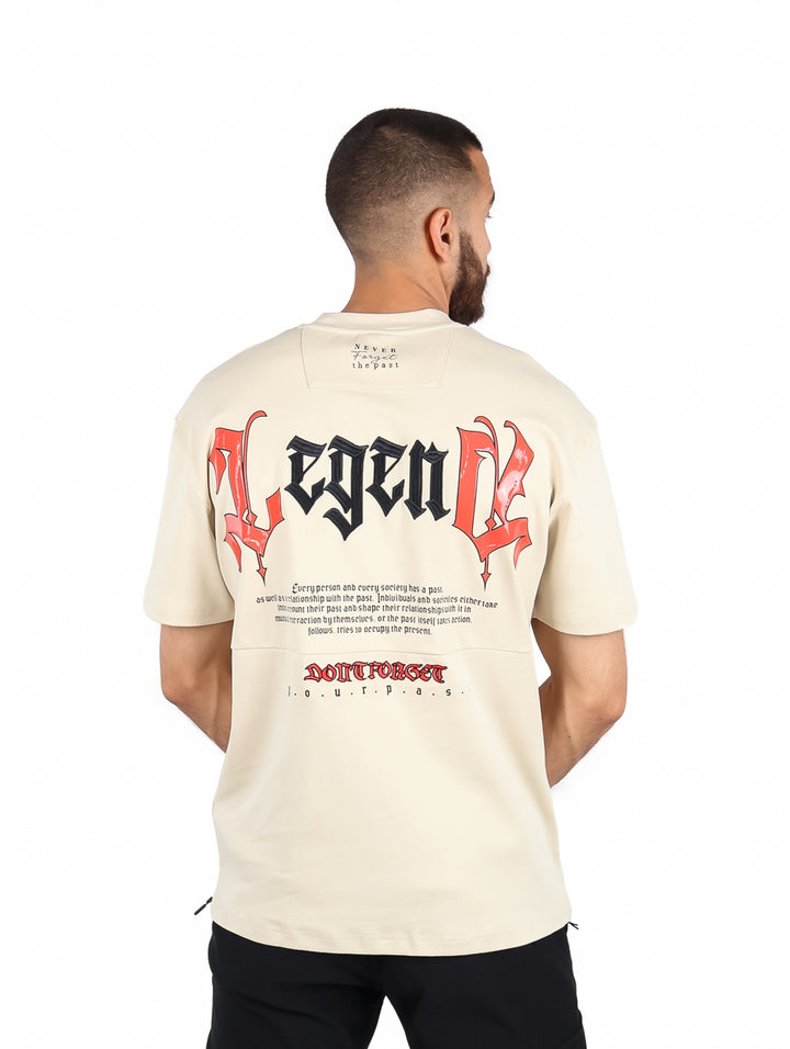 Hombre vistiendo una playera de color beige de manga corta con un pequeño logo rojo en el pecho.