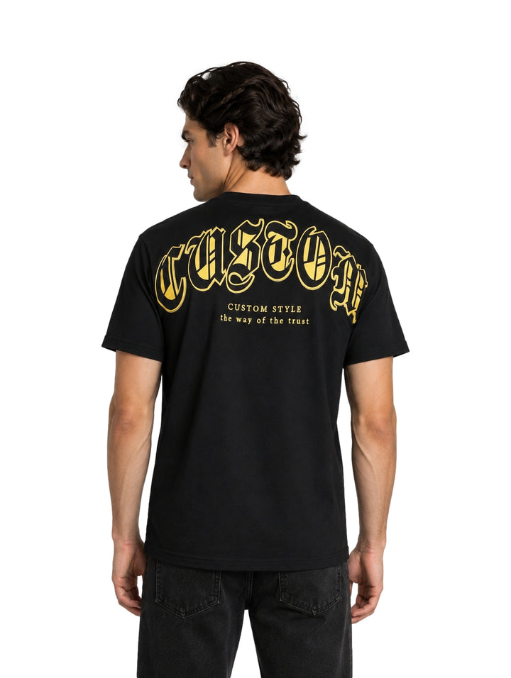 Hombre vistiendo playera negra de manga corta con estampado dorado en el pecho.