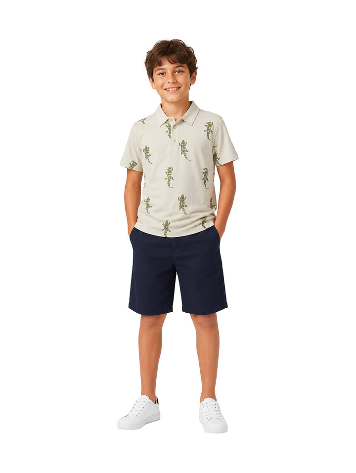 Niño vistiendo un conjunto de polo beige con estampado de lagartos y short azul marino.