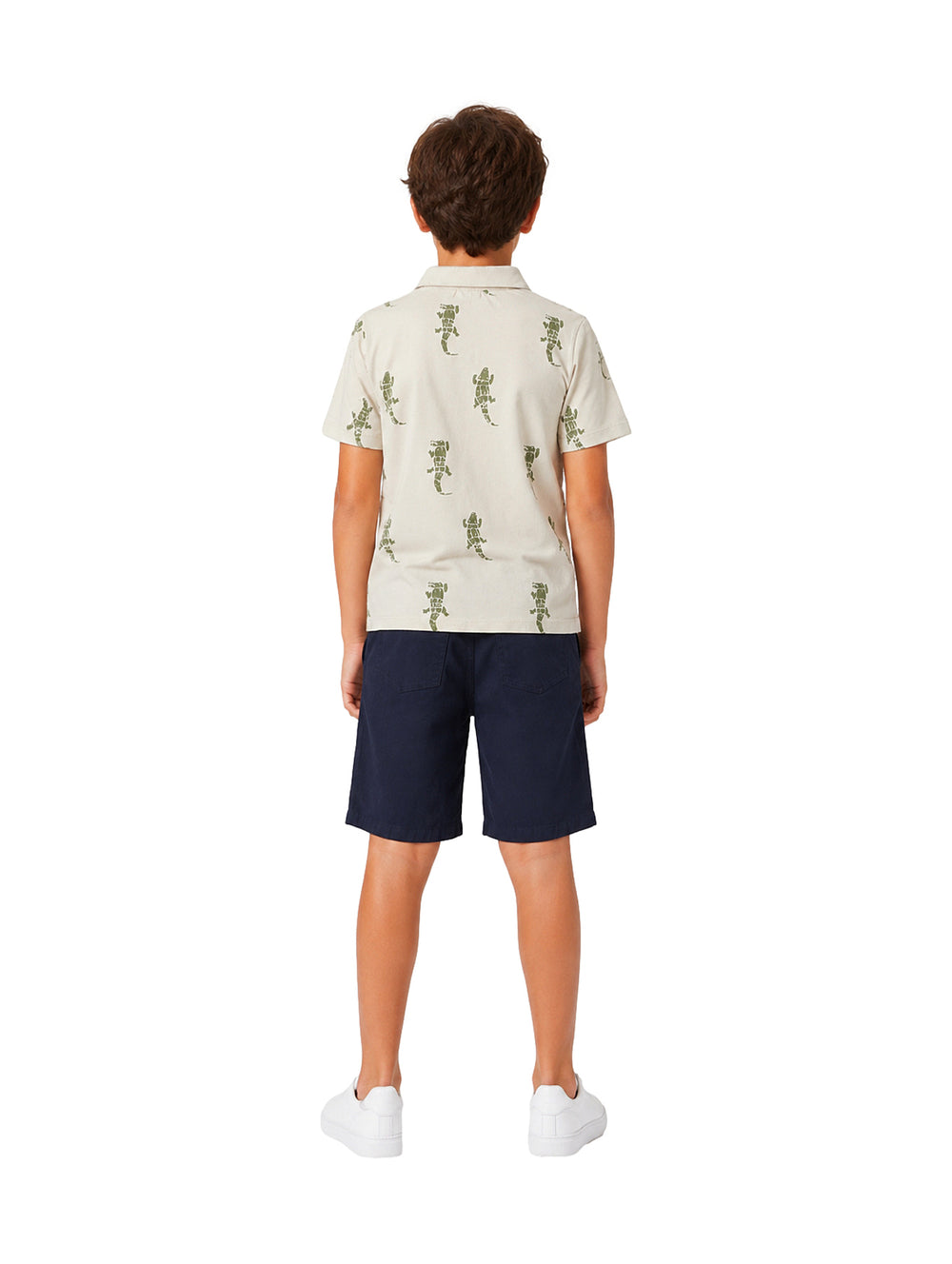 Niño vistiendo un conjunto de polo beige con estampado de lagartos y short azul marino.