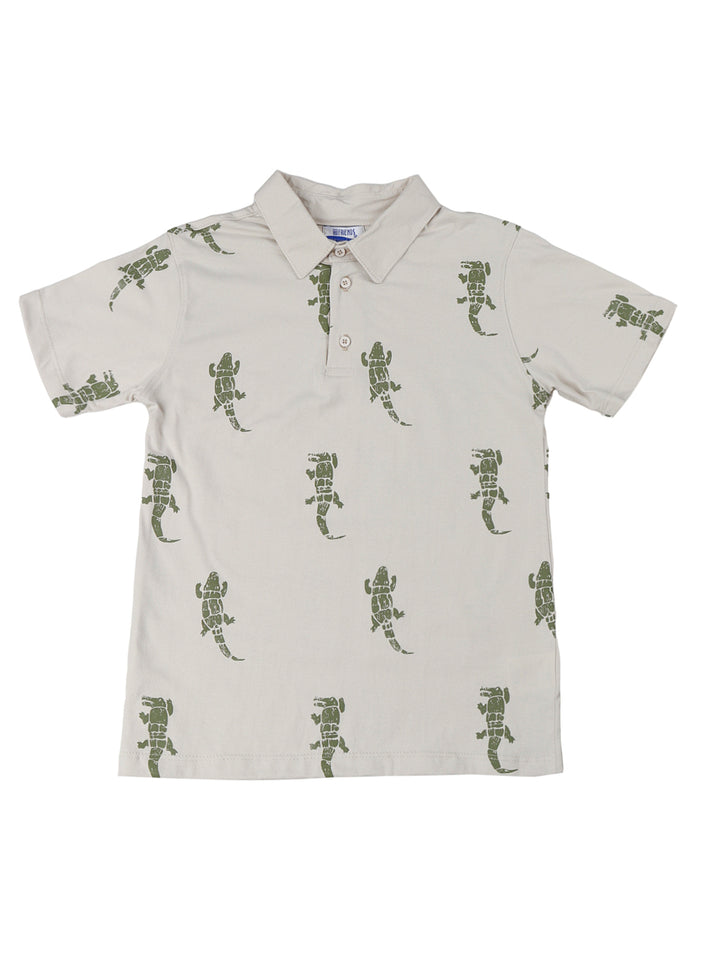 Niño vistiendo un conjunto de polo beige con estampado de lagartos y short azul marino.