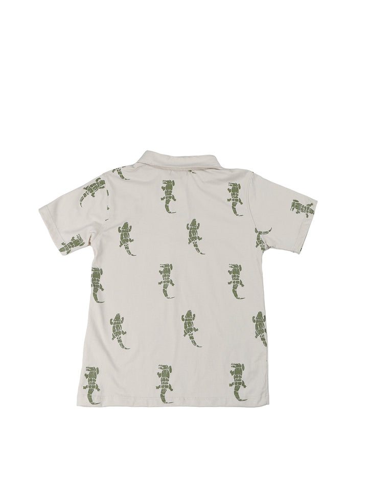Niño vistiendo un conjunto de polo beige con estampado de lagartos y short azul marino.