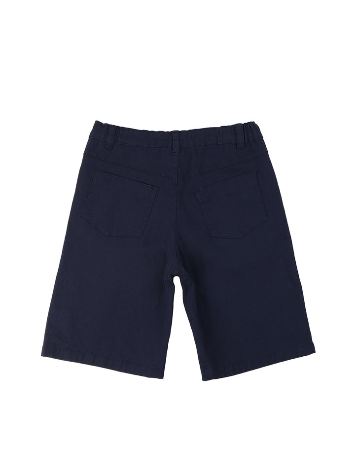 Niño vistiendo un conjunto de polo beige con estampado de lagartos y short azul marino.