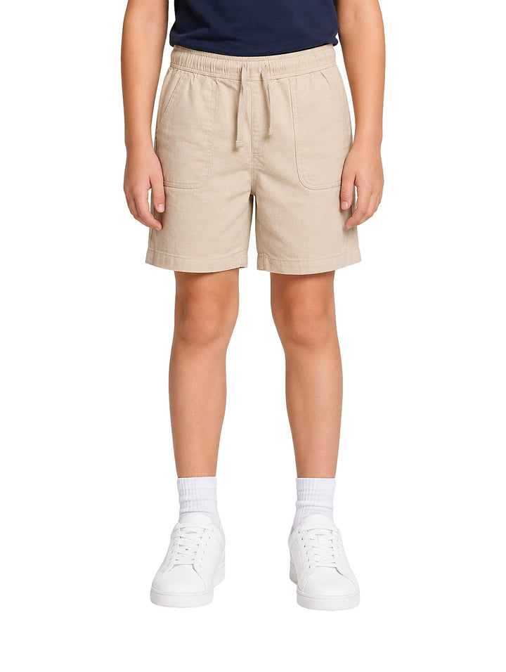 Niño vistiendo un short color beige con cintura elástica y tenis blancos.