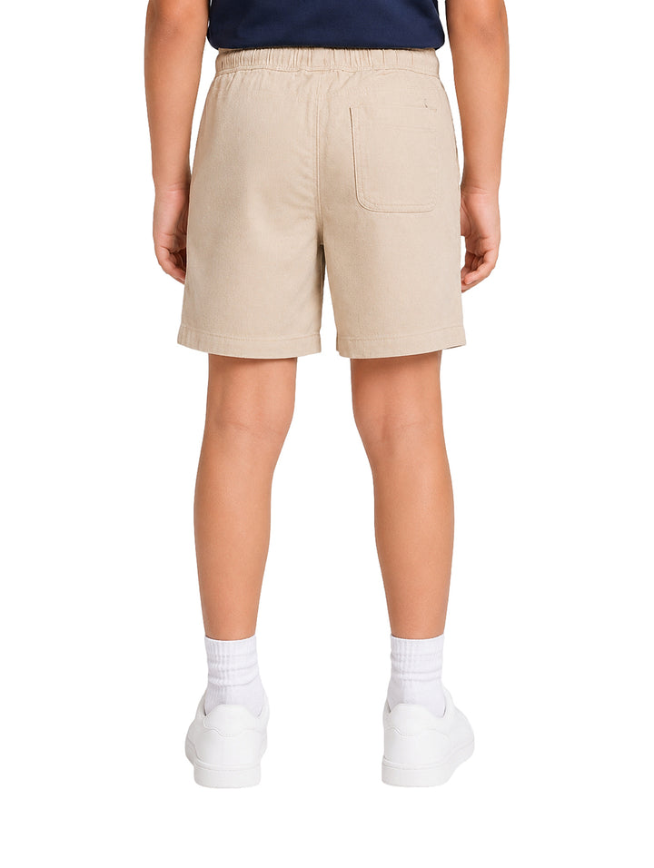 Niño vistiendo un short color beige con cintura elástica y tenis blancos.