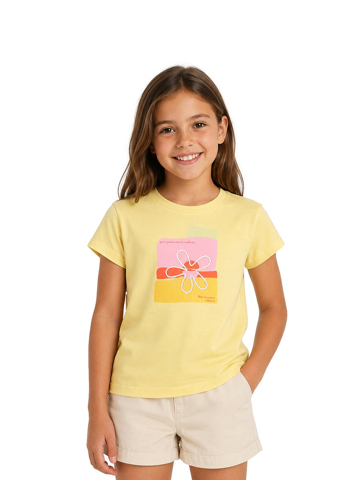 Niña vistiendo una camiseta amarilla de manga corta con estampado floral colorido y shorts beige.