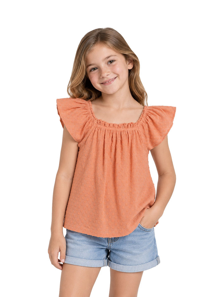 Niña vistiendo una blusa color naranja claro con textura y volantes en los hombros, combinada con shorts de mezclilla.