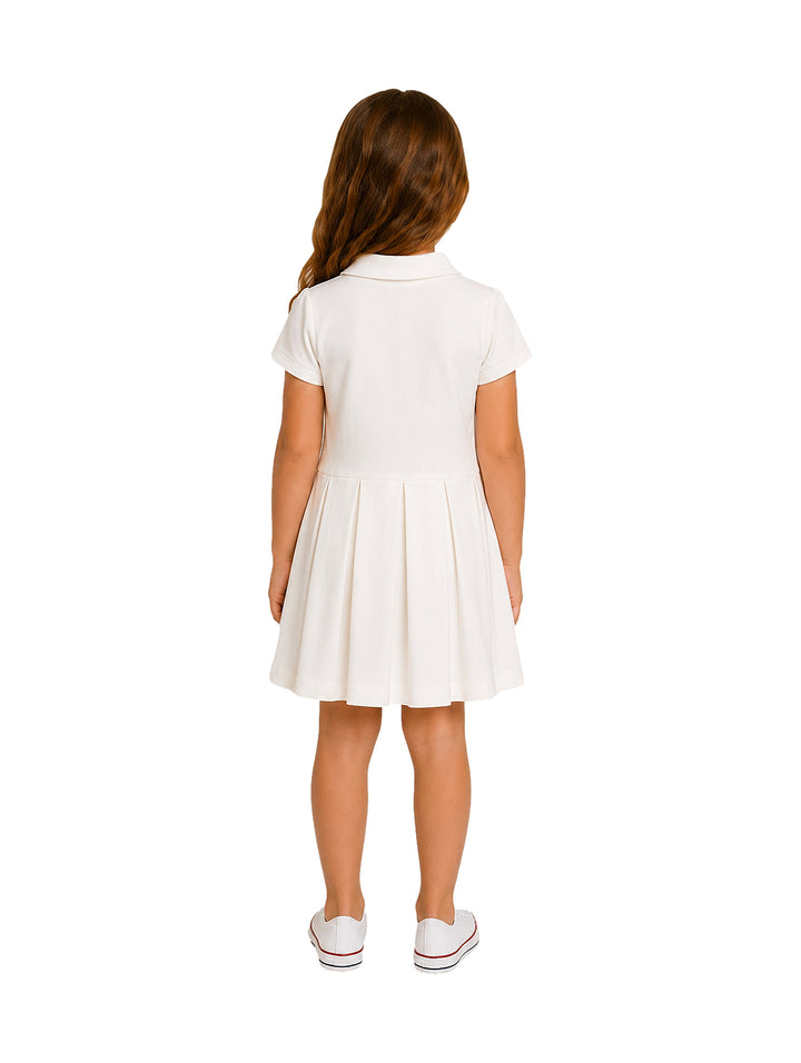 Niña vistiendo un vestido color ivory de manga corta con cuello polo y falda plisada.