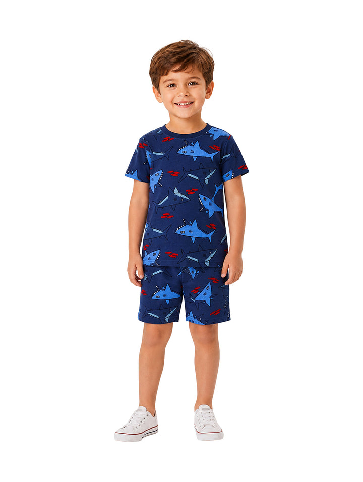 Niño vistiendo conjunto de camiseta y shorts azules con estampado de tiburón y tenis blancos.