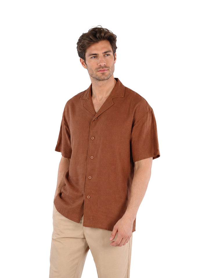 Hombre vistiendo una camisa de manga corta color café con botones y cuello abierto.