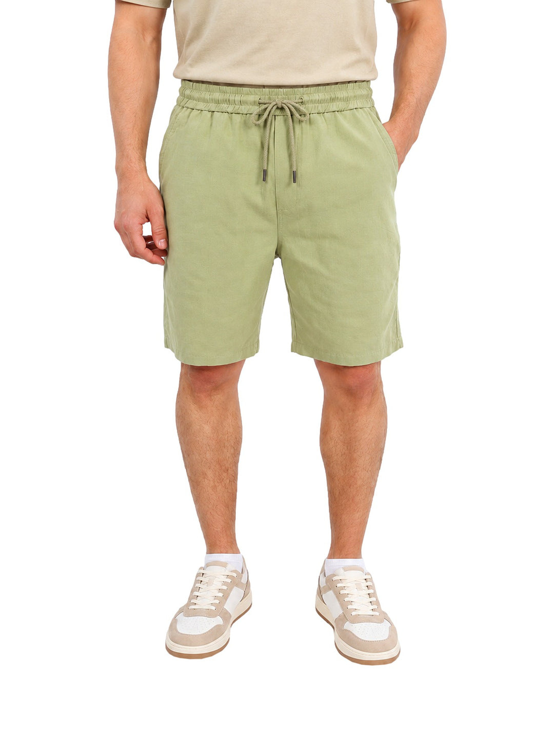 Hombre vistiendo short corto color verde con jareta en la cintura y calzado casual blanco.