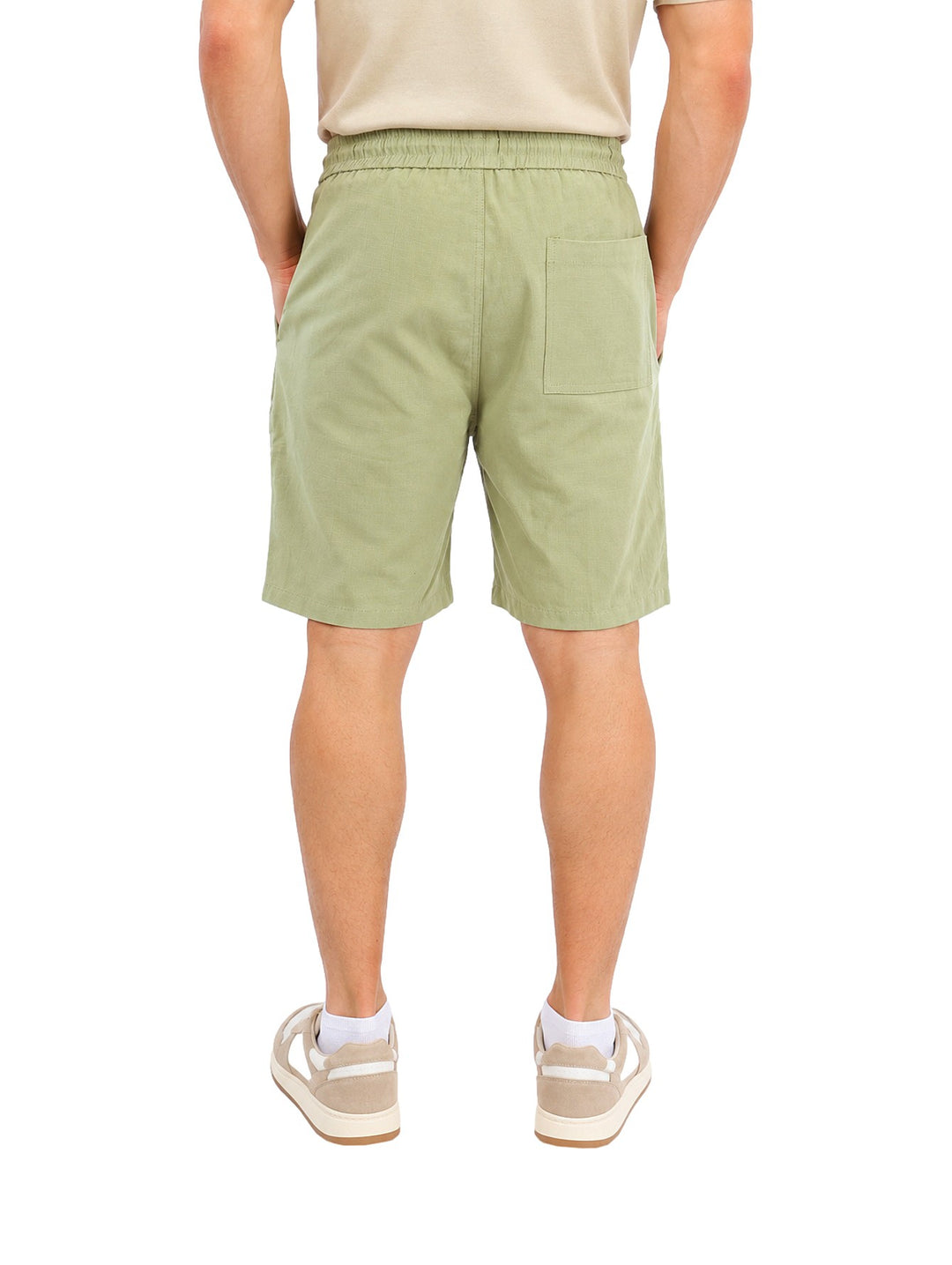 Hombre vistiendo short corto color verde con jareta en la cintura y calzado casual blanco.
