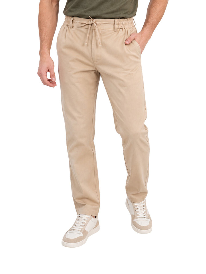 Hombre vistiendo pantalón elástico color beige de corte recto con cordón en la cintura.