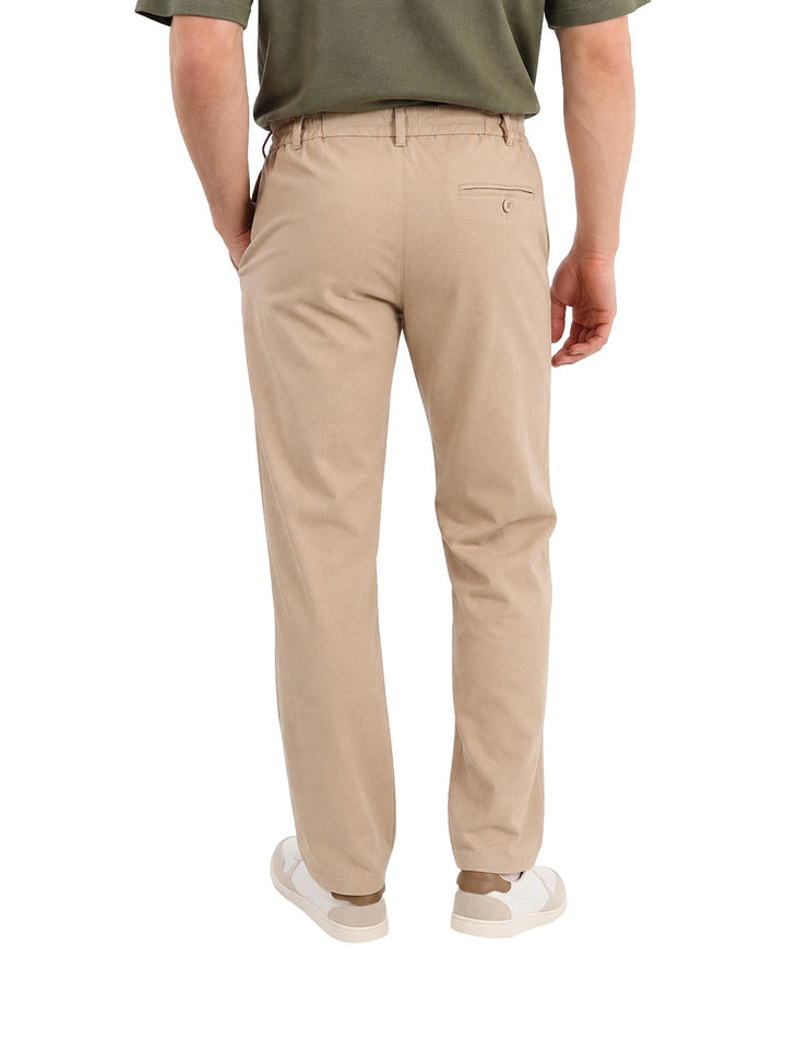 Hombre vistiendo pantalón elástico color beige de corte recto con cordón en la cintura.