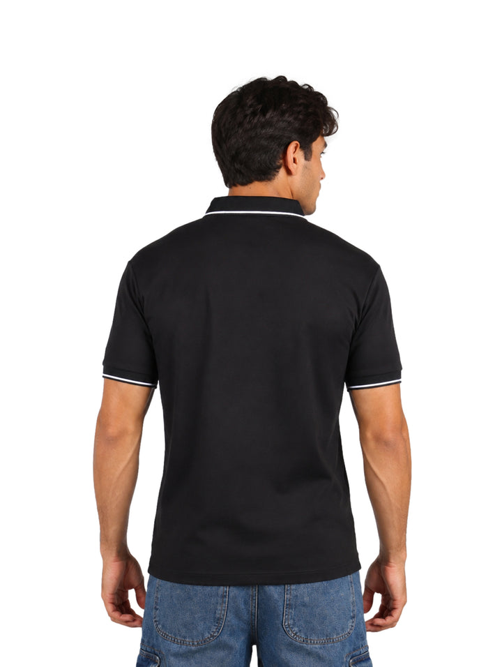 Hombre vistiendo una playera polo color negro con detalles blancos en el cuello y los bordes de las mangas.