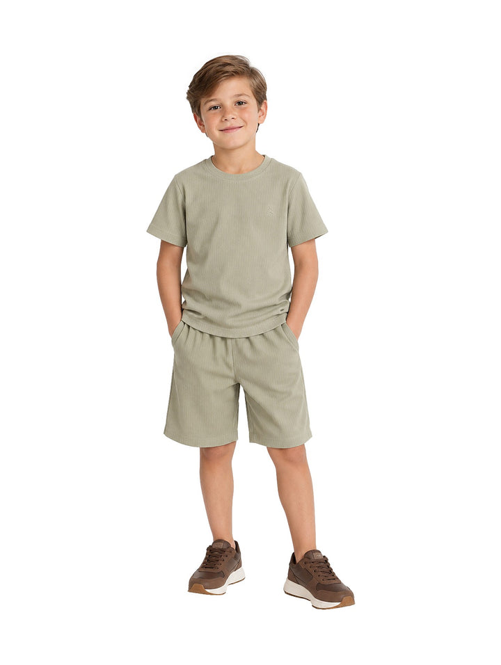 Niño vistiendo un conjunto de camiseta y short en color verde militar con tenis marrones.
