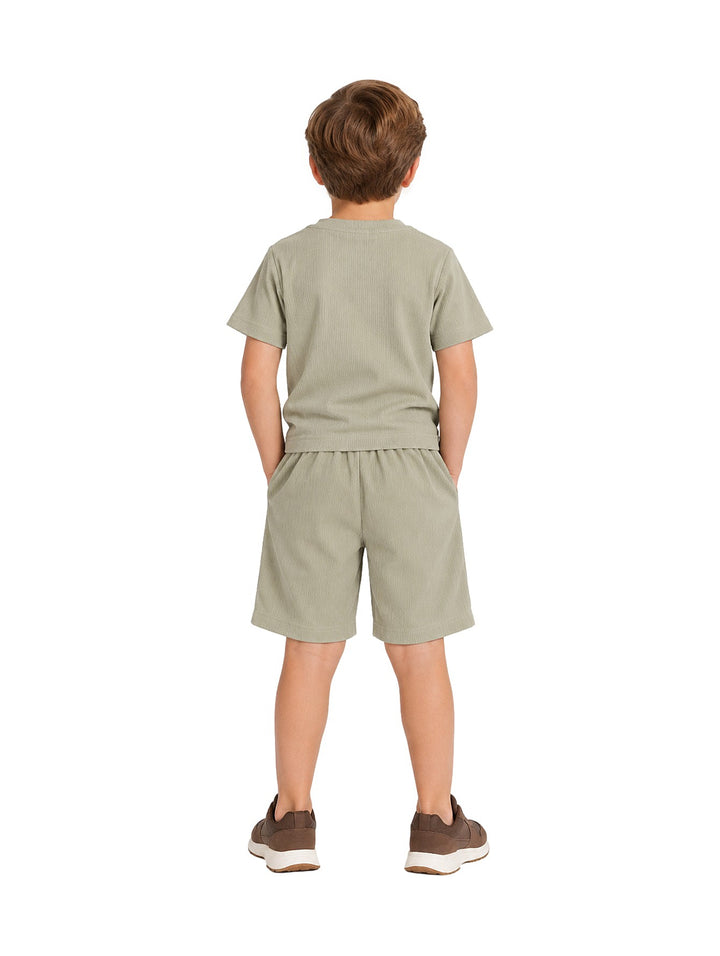 Niño vistiendo un conjunto de camiseta y short en color verde militar con tenis marrones.