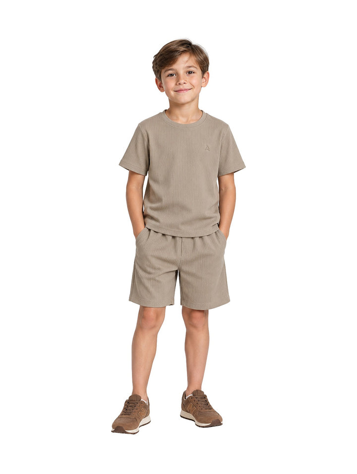 Niño vistiendo un conjunto de camiseta y short en color verde claro con textura acanalada y tenis marrones.