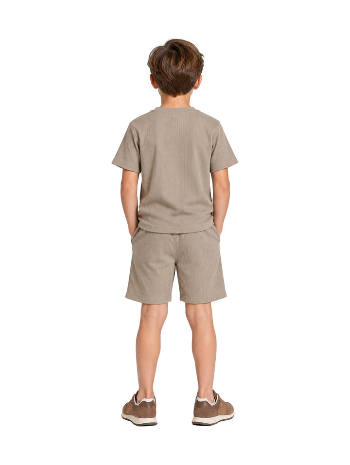 Niño vistiendo un conjunto de camiseta y short en color verde claro con textura acanalada y tenis marrones.