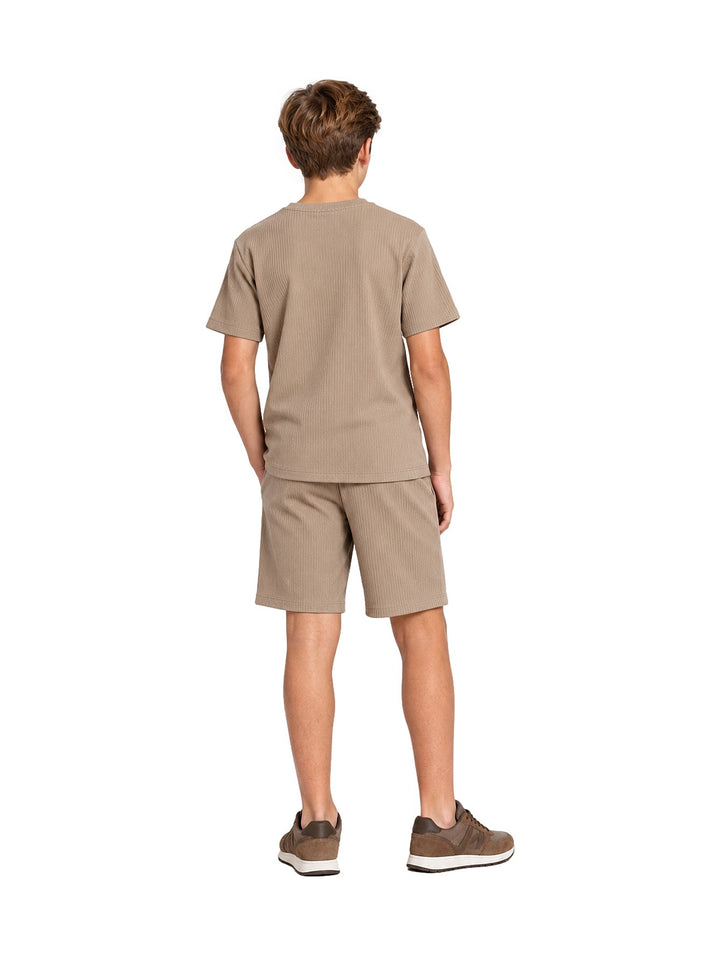 Niño vistiendo un conjunto casual de camiseta y shorts color khaki con tenis marrones.