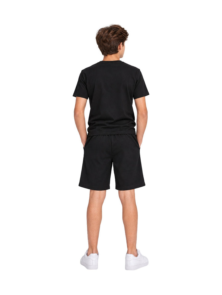 Niño vistiendo un conjunto de camiseta y shorts color negro de la marca ATOK con tenis blancos.
