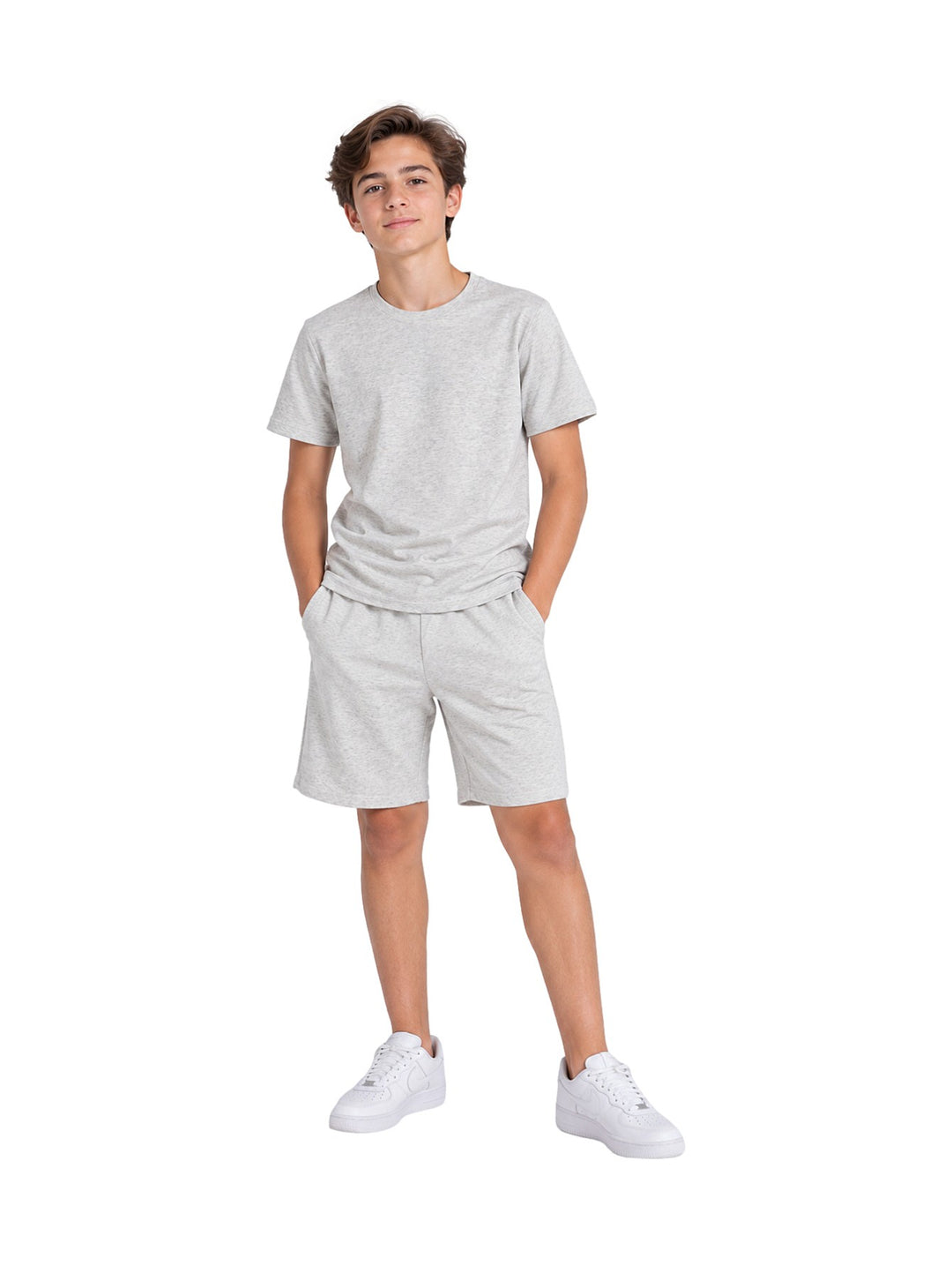 Niño vistiendo un conjunto casual de camiseta y short en color gris claro con tenis blancos.