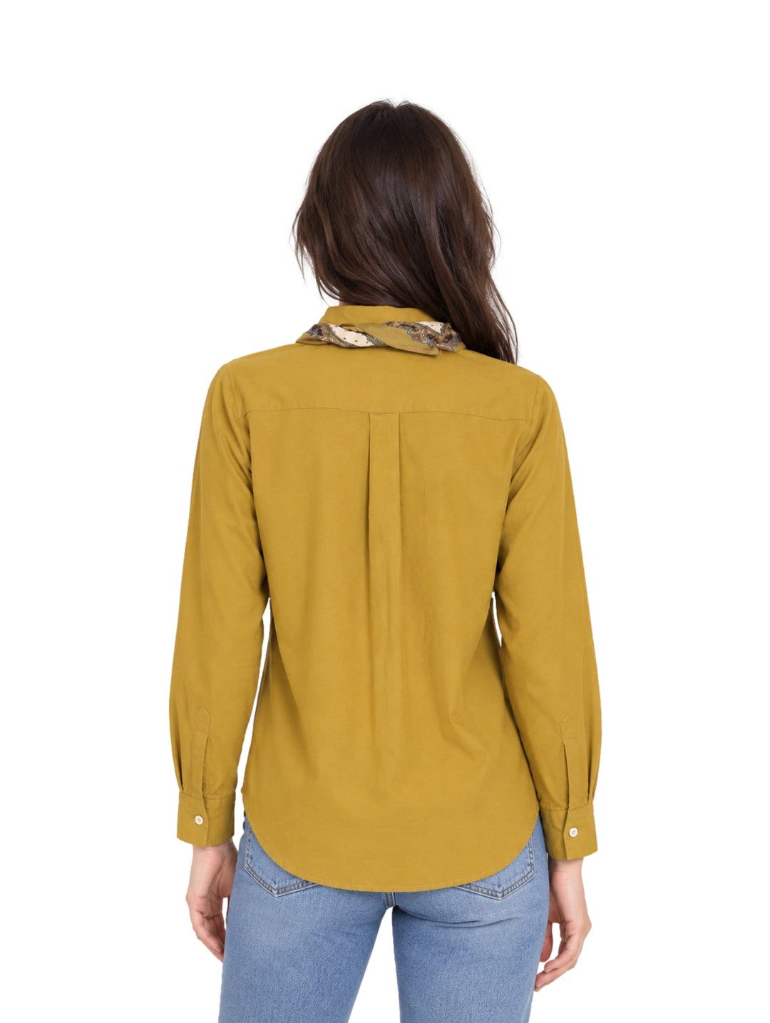 Mujer vistiendo una camisa color mostaza de manga larga con un pañuelo al cuello y jeans azules.
