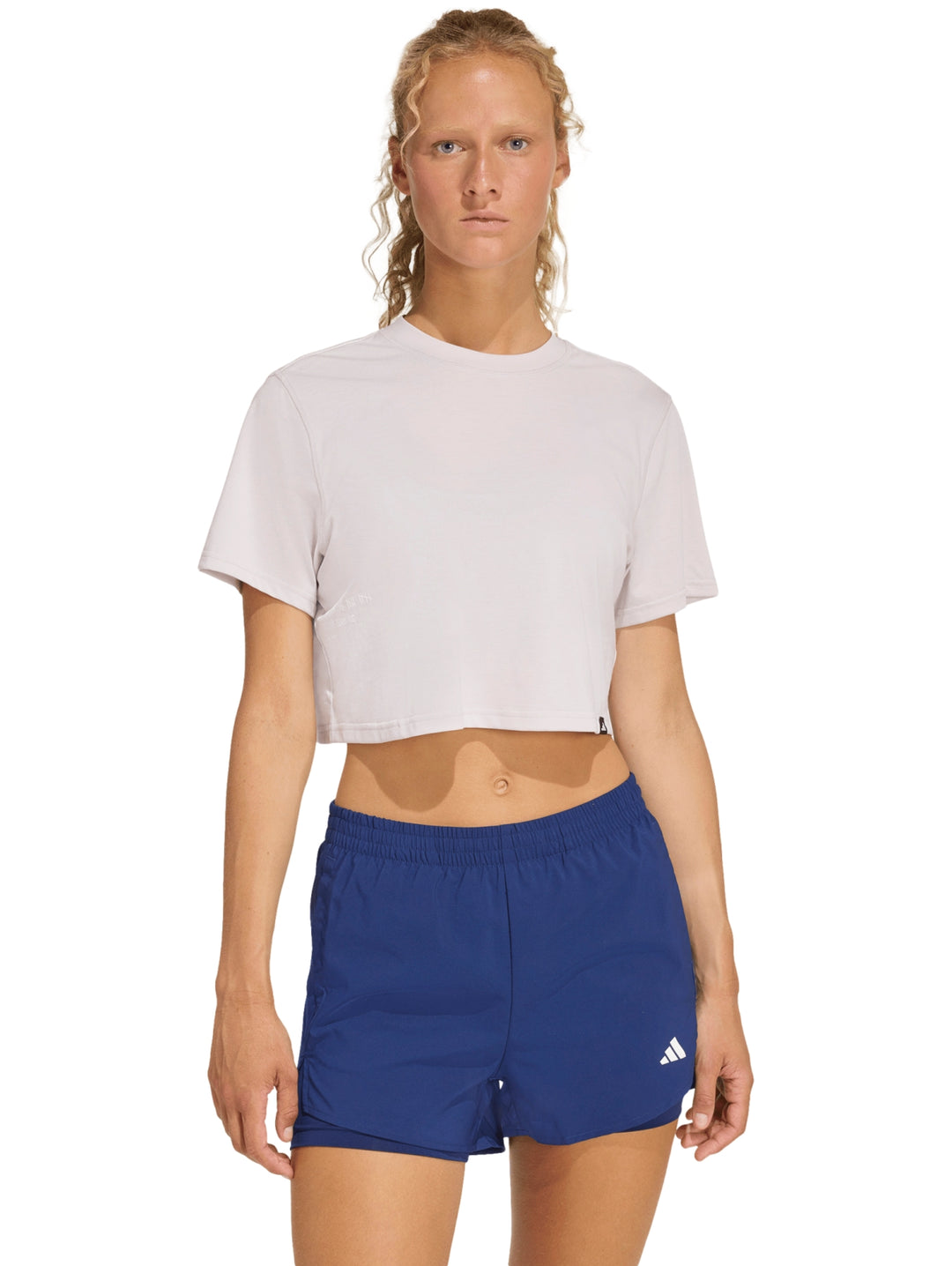 Mujer modelando una camiseta deportiva corta color violeta claro de la marca Adidas.